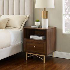 a nightstand with a lamp on top of it next to a neatly made bed in a bedroom