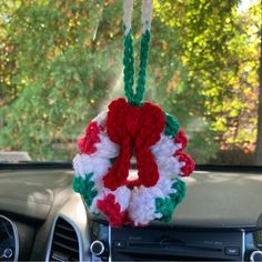 a crocheted christmas wreath hanging from the dashboard of a car with trees in the background