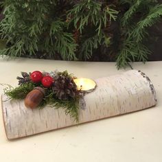 a candle is sitting on top of a piece of wood with pine cones and berries