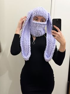 a woman wearing a purple knitted mask and holding a cell phone in front of her face