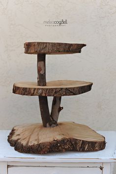 a three - tiered tree slice cake stand on top of a white table with a wall in the background