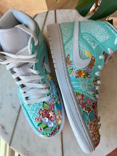 Step into a world of artistry with "Blossom", a stunning reinvention of the iconic Air Jordan 1 Highs. Hand-painted in a refreshing mint greenish-blue base, these sneakers bloom with vibrant multicolor florals, making each pair a wearable garden of creativity. Neha Assar’s signature touch extends to customized details and intricate embellishments, adding subtle elegance to every inch of the design. Whether you’re looking to elevate your streetwear game or make a statement with bold, artistic footwear, Blossom is the perfect blend of sophistication and edge. These sneakers are made for those who walk with confidence and appreciate the beauty in every detail. • Hand-Painted & One-of-a-Kind: No two pairs are the same, offering a unique floral story. • Artful Embellishments: Thoughtfully curat Designs To Draw On Shoes, Hand Painted Sneakers, Nike Custom, Painted Nikes, Air Jordan 1s, Painted Sneakers, Creative Shoes, Walk With Confidence, Sneaker Design