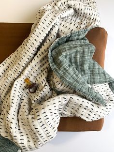 an unmade bed with white and green sheets on it, next to a brown pillow