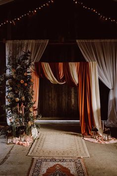 a decorated stage with drapes and flowers on the floor, surrounded by candles and rugs