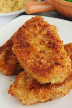 three pieces of fried food on a white plate next to some vegetables and other foods