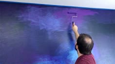 a man painting a wall with purple paint