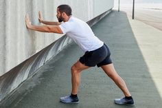 a man leaning against a wall and stretching his arms to reach the ground with one hand