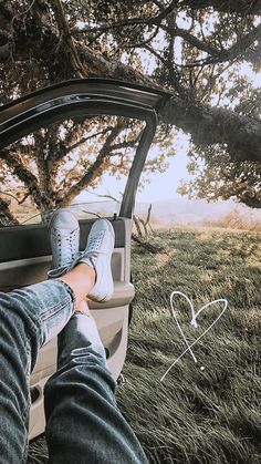 someone's feet sticking out the window of a car in front of a tree