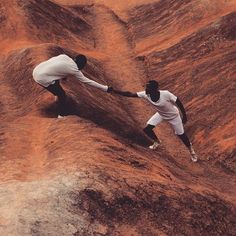 two men in white shirts and black pants are holding hands on top of some dirt