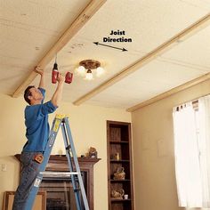 a man on a ladder painting the ceiling in his living room with red mason jars