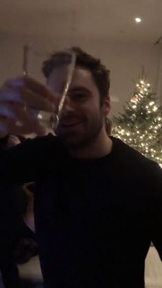 a man standing in front of a christmas tree holding a wine glass up to the camera