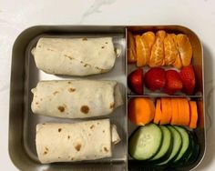 an open lunch box with fruit, vegetables and tortilla wraps in it