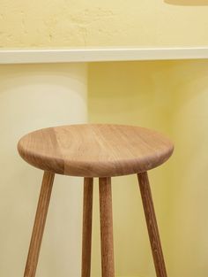 a wooden stool sitting on top of a hard wood floor next to a yellow wall