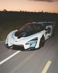 a white and blue sports car driving down the road at sunset or dawn with trees in the background