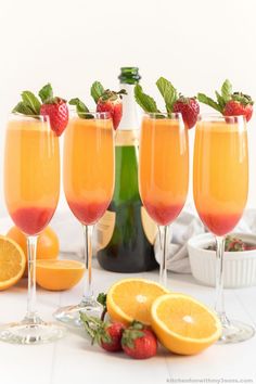 three glasses filled with orange juice and garnished with strawberries next to sliced lemons