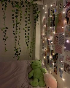 a green teddy bear sitting on top of a bed next to a wall covered in pictures