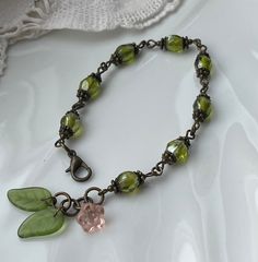 a bracelet with green leaves and a pink flower charm on an antique bronze plated chain