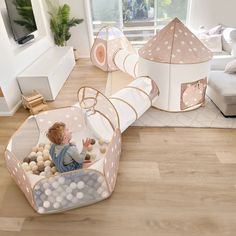 a baby sitting in a play tent with balls and rocks on the floor next to it