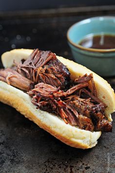 a roast beef sandwich on a bun next to a bowl of chocolate sauce and spoon