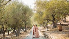 a bride and groom walking down a path in the middle of an olive grove during their wedding day