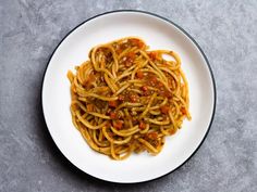 a white plate topped with spaghetti covered in sauce and chili paste on top of a gray table