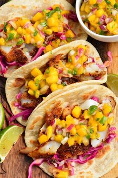 fish tacos with corn and slaw on a cutting board next to lime wedges