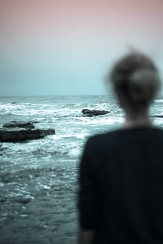 a person standing in front of the ocean looking out at the water and rocks on the shore