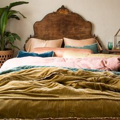 a bed with pillows and blankets on top of it in a bedroom next to potted plants