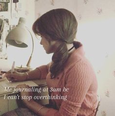 a woman sitting at a desk in front of a lamp and writing on a piece of paper