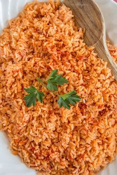 a white plate topped with rice and parsley next to a wooden spoon on top of a table