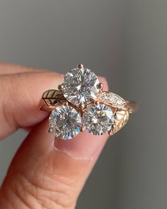 a woman's hand holding an engagement ring with three stone flowers on the side