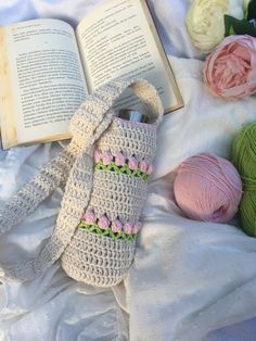 a crocheted book bag sitting on top of a bed next to balls of yarn