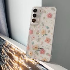 an iphone case sitting on top of a window sill with flowers and glitters