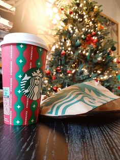 a starbucks cup sitting on top of a wooden table next to a bag and christmas tree