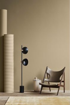 a chair and lamp in front of a beige wall with a brown rug on the floor