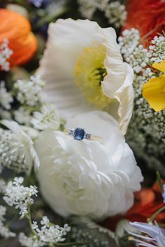 an engagement ring sitting on top of white and yellow flowers with other flowers in the background