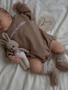 a baby laying on top of a bed holding a stuffed animal