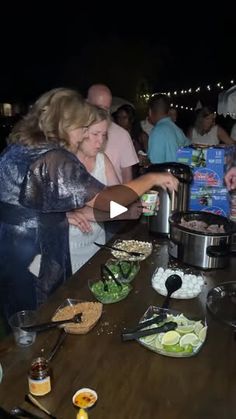 a group of people standing around a table with food on it