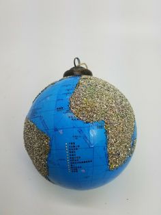 a blue and gold globe ornament on a white surface with silver glitters