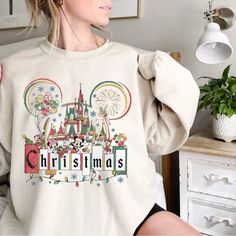 a woman is sitting on a bed wearing a mickey mouse christmas sweatshirt with the word disney written in front of her