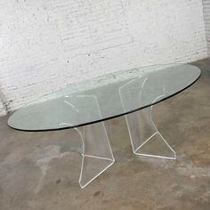 an oval glass table with metal legs in front of a white brick wall and floor