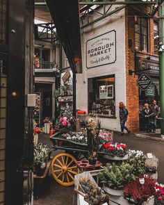 an outdoor market with lots of flowers and plants on the sidewalk in front of it