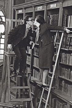 an old photo of two people kissing each other on the stairs in front of a bookshelf