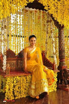 a woman sitting on top of a wooden bench covered in yellow flower garlands and flowers