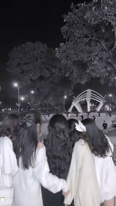 group of young women standing together in front of a tree and bridge at night time