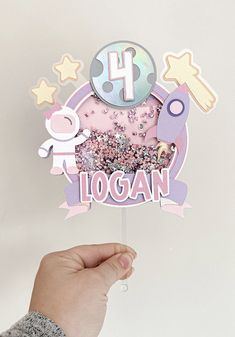 a hand holding up a pink and purple cake topper with the number four on it