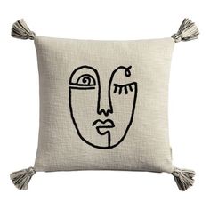 a pillow with a face drawn on the front and tassels around the edges