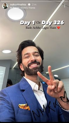 a man in a blue suit making the peace sign with his hand and smiling at the camera