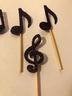 three sticks with music notes on them sitting next to each other, one is made out of wood and the other has black glitter