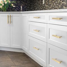 a kitchen with white cabinets and gold pulls on the handles, along with flowers in a vase